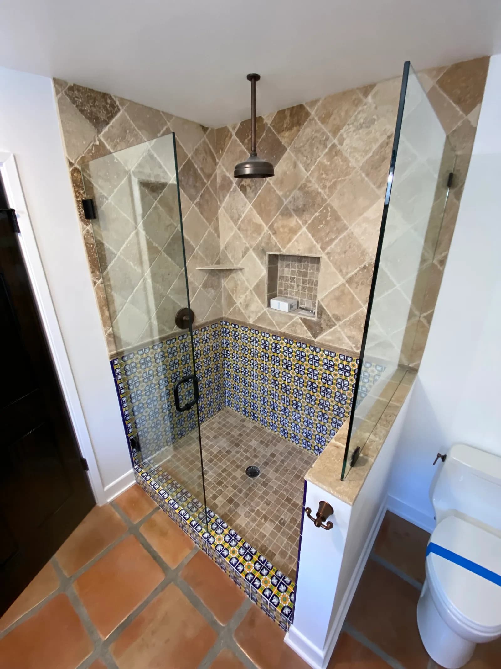 Custom walk-in shower with travertine and Talavera tile, frameless glass, and dark stained door in Santa Barbara, CA