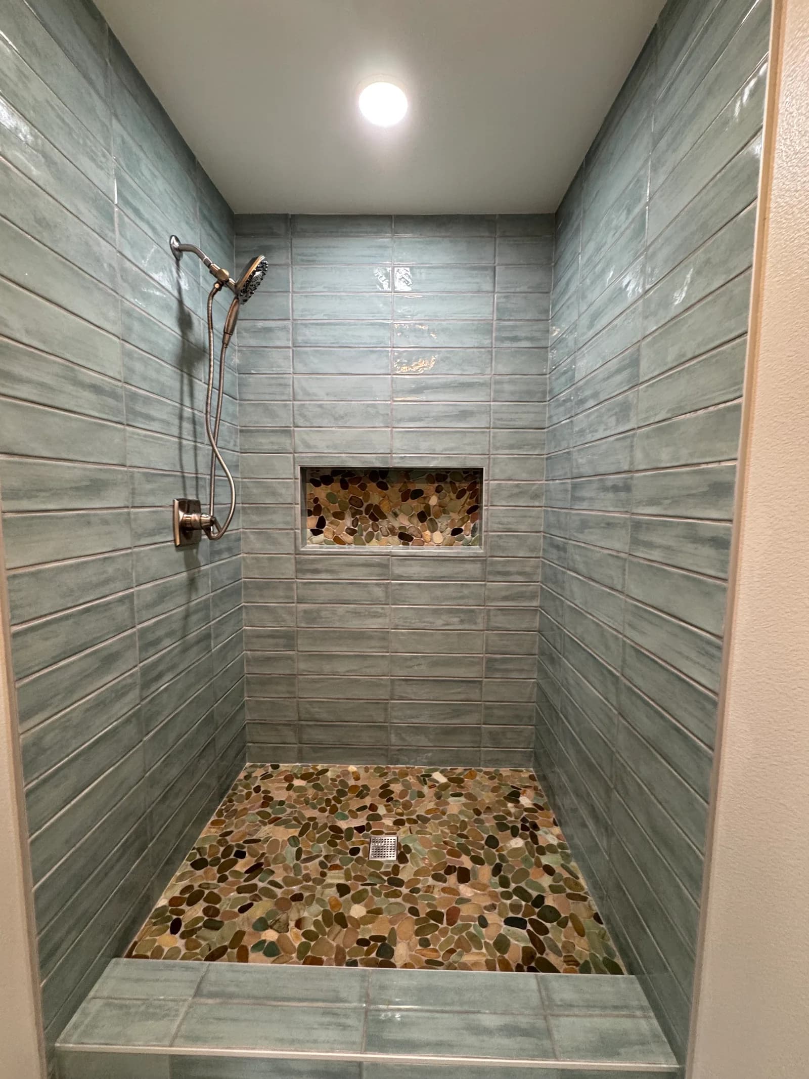 Custom walk-in shower with vertical plank tile walls and natural pebble tile floor and niche in Somis, CA
